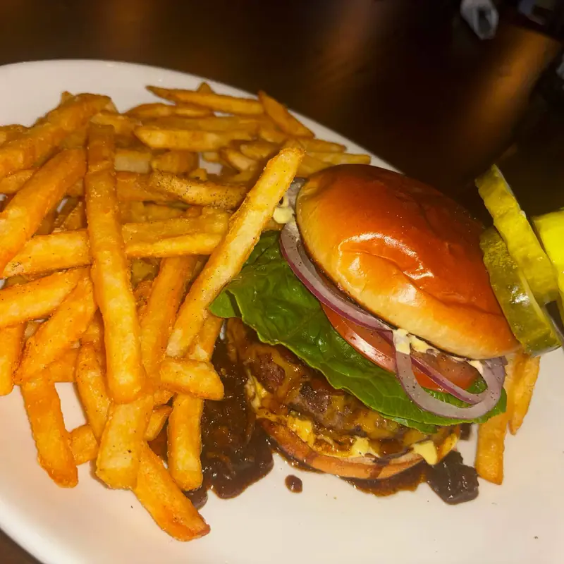 A cheeseburger on a brioche bun with lettuce, tomato and red onion, served with seasoned fries and a pickle