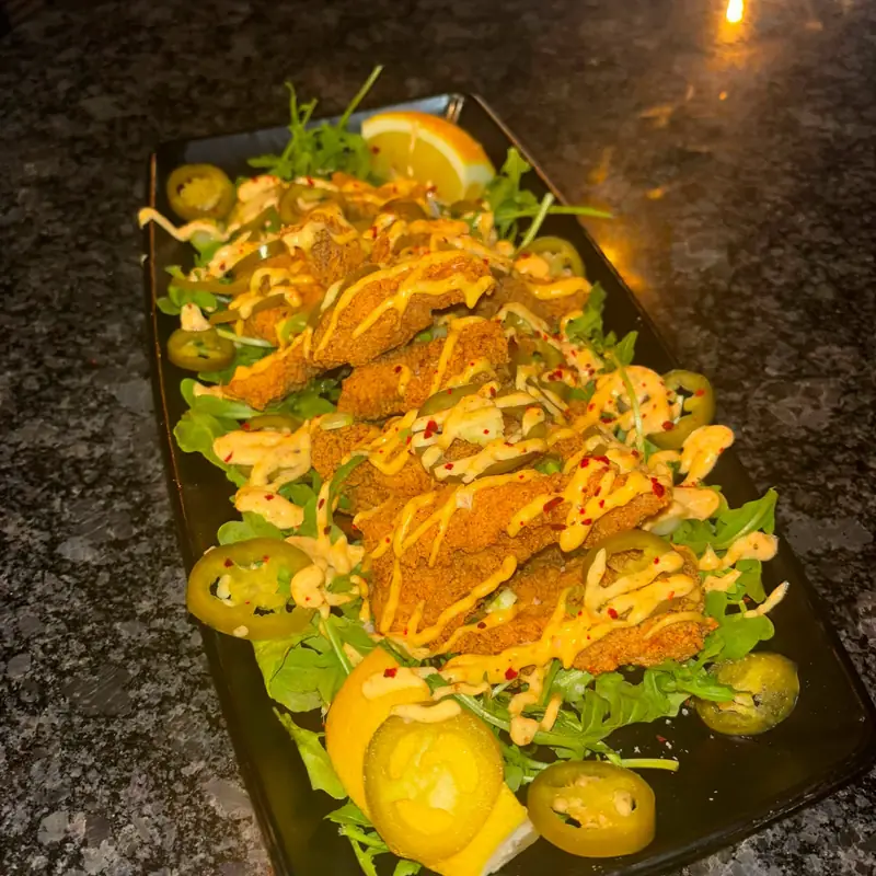 Crispy fried chicken strips over arugula with pickled jalapeños and a spicy aioli drizzle