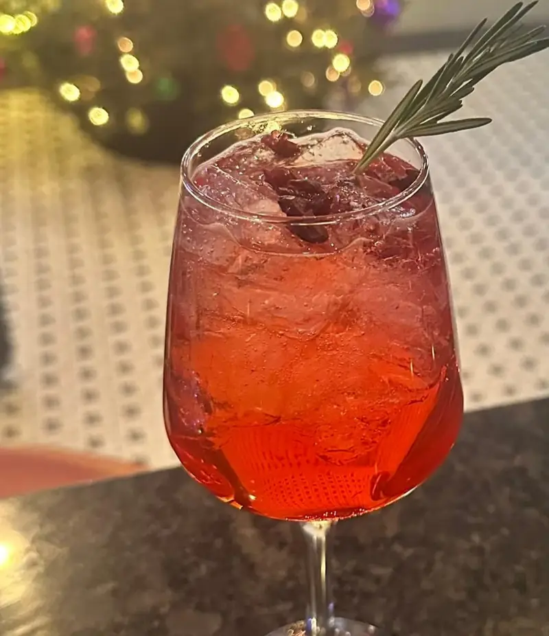 A cranberry spritz over crushed ice with a fresh rosemary sprig
