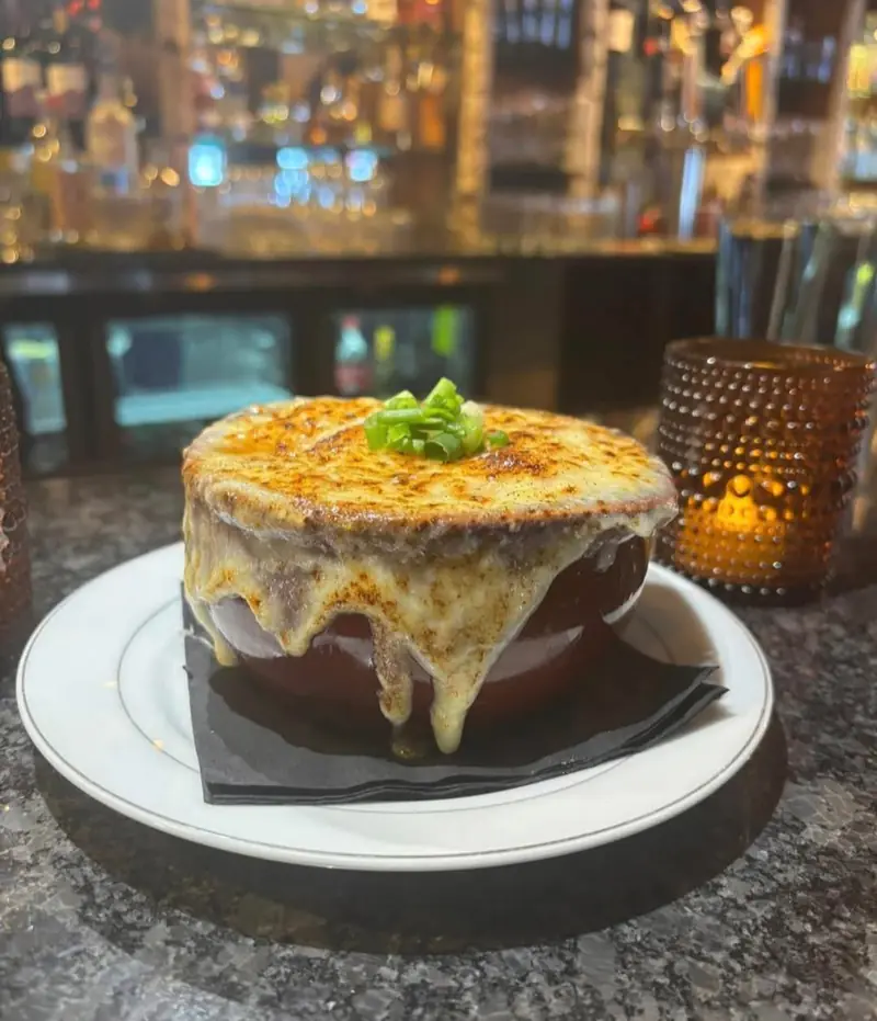 French onion soup — broiled cheese crust melting down the crock, topped with scallions, in the candlelit bar