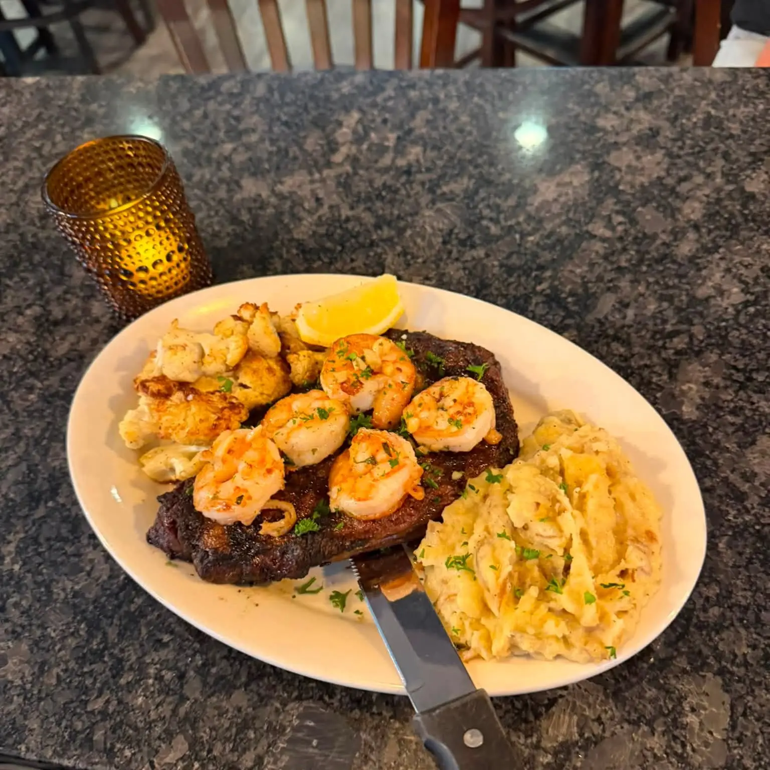 A grilled ribeye topped with garlic-butter shrimp scampi and garlic mashed potatoes.