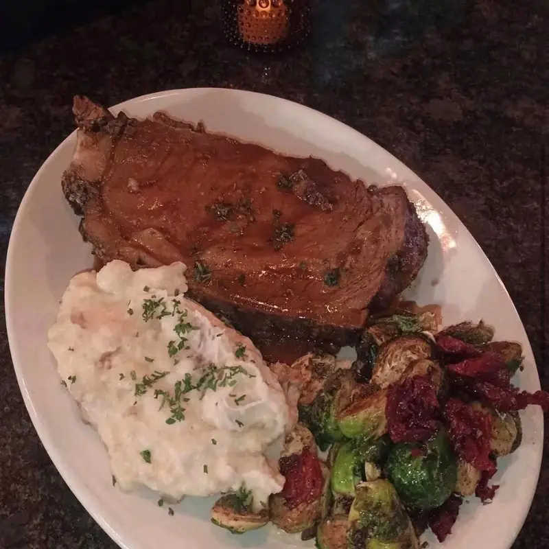 A slow-roasted prime rib plated with garlic mashed potatoes and balsamic-glazed Brussels sprouts