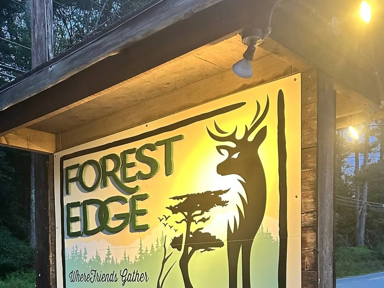 The Forest Edge sign lit gold at dusk along Route 590 — a stag and pines silhouetted against the Pocono woods.